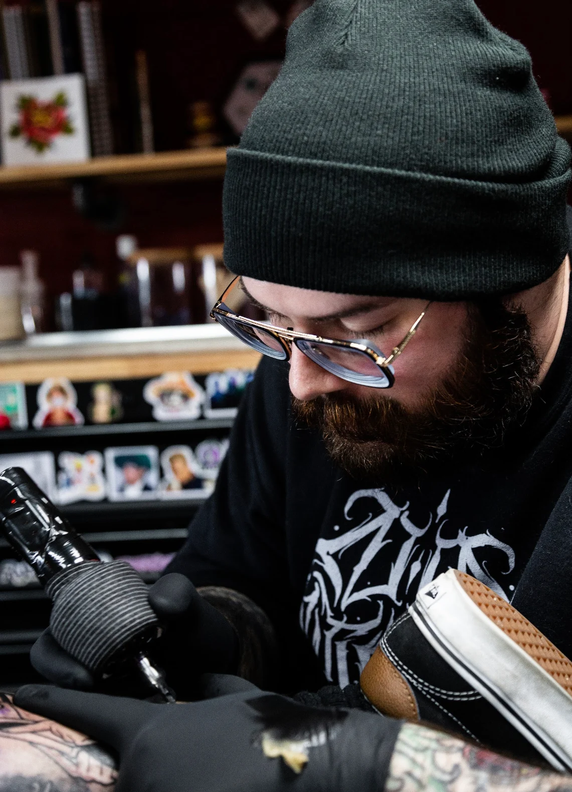 Jade, wearing a beanie and glasses, working on a tattoo
